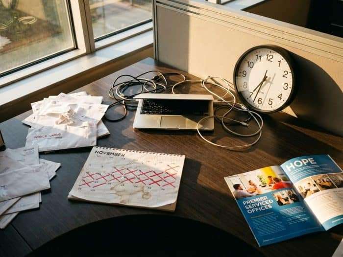 Modernt kontorsskrivbord ovanifrån med laptop, obetalda fakturor, fläckad kalender och broschyr för serverat kontor