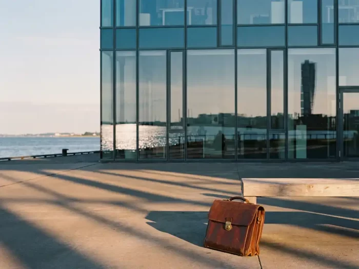 Professionell portfölj på bänk framför modernt glaskontor med Öresund och Turning Torso i bakgrunden, Malmö