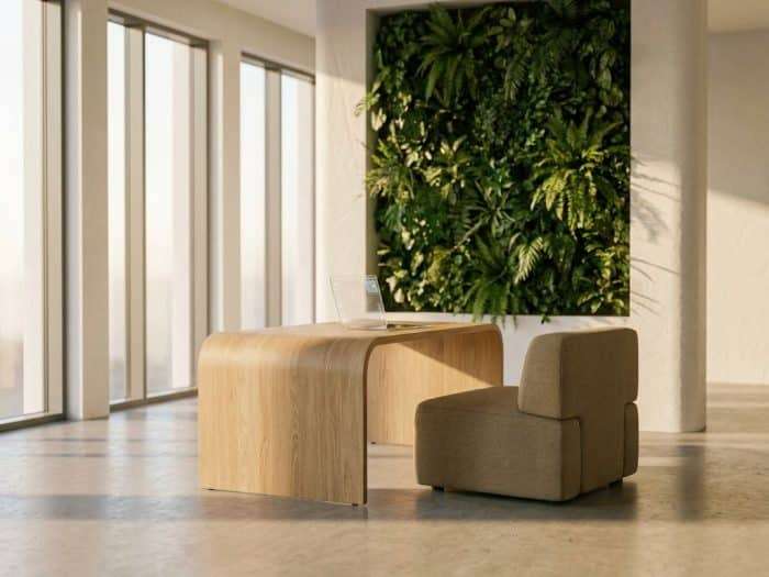 Minimalistiskt kontorsarbetsområde med ergonomiskt skrivbord i ljust trä, växtvägg och naturligt dagsljus genom fönster